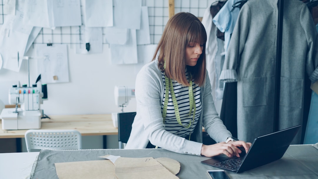 Young female owner of small tailor's shop is working with laptop in her workplace. She is ordering fabric for new collection from local textile supplier. Successful start-up concept.