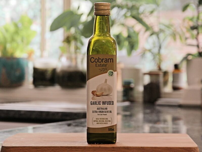 Fles olijfolie met etiket naast olijven op een houten keukenblad